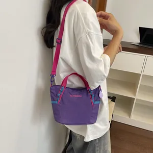Detailed shot of a stylish purple and pink nylon crossbody bag worn by a model in white