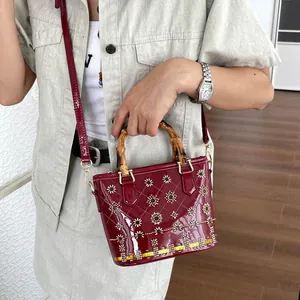 Detail of a dark red patent leather bucket bag with bamboo handles on a model