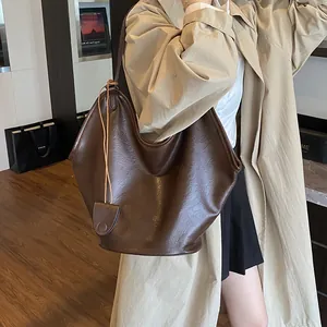 Large brown faux leather hobo underarm bag shown on a model wearing a classic trench coat
