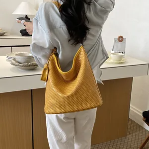 Large capacity yellow woven hobo bag worn by a model in a modern cafe setting.