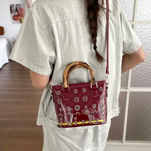 Close-up of burgundy patent leather bag with bamboo handle and sequin floral details