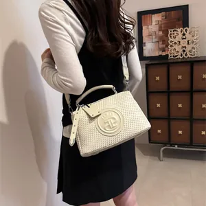 Elegante cremefarbene gewebte Handtasche, getragen von einem Modell in Innenräumen.