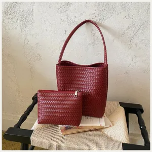 Bolso tipo cubo trenzado rojo con neceser a juego sobre silla de paja
