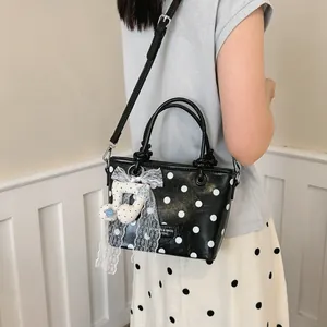 Detail view of a stylish black polka dot handbag with lace bow and musical note charm.