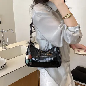 Close-up of black crocodile embossed baguette bag with colorful bead charm on a model