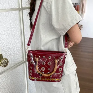Detailed view of burgundy patent leather bucket bag with bamboo handles and beadwork
