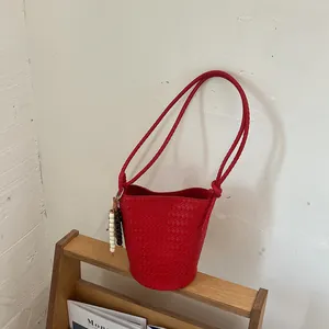 Detailaufnahme eines roten geflochtenen Beuteltasche mit Schultergurt auf einem Regal