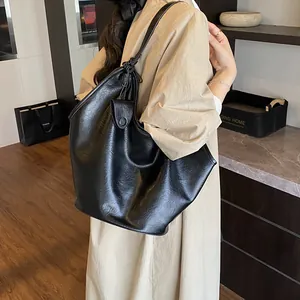 Close-up of large black slouchy leather tote bag worn over the shoulder by a female model.