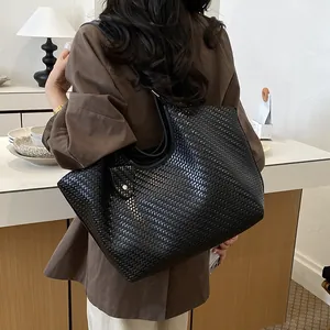 Close-up of a large black woven shoulder tote bag with texture detail worn by a model