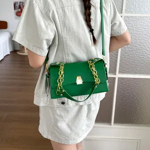 Green rectangular crossbody bag with gold chain and unique trapezoid buckle worn by model