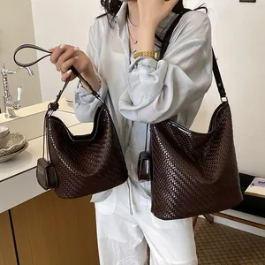 Model carrying two brown woven hobo bucket bags in a lifestyle bathroom setting