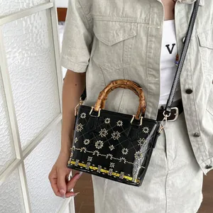 Detail of black patent leather bucket bag with bamboo handle and floral embroidery.
