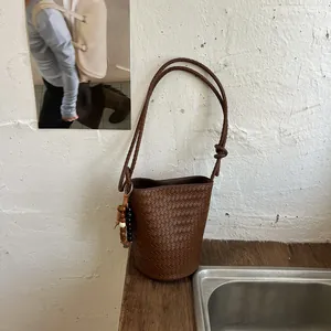 Detailansicht einer stilvollen braunen geflochtenen Eimertasche mit Perlenanhänger und Knoten