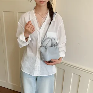 Light blue women's bucket bag with knotted handles worn as a crossbody