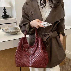 Close-up detail of a burgundy woven tote bag held by a model in a stylish brown coat.