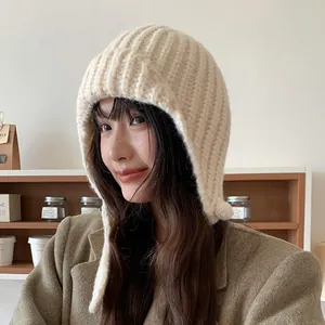 Warme cremefarbene Strickmütze mit Ohrenklappen für den Winter am asiatischen Model.