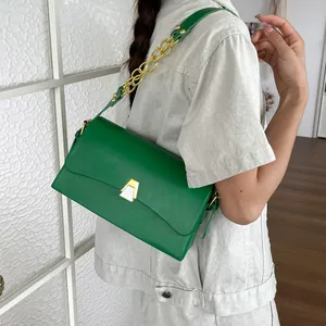Detail of a vibrant green leather shoulder bag with gold chain strap worn by a model