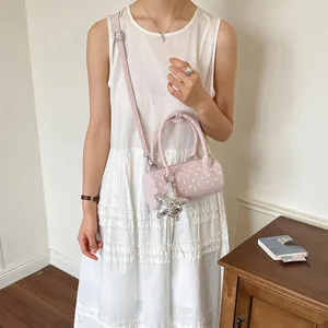 Close-up of pink polka dot cylinder handbag worn by model in white dress