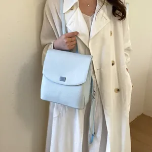 Elegant light blue minimalist backpack shown worn with a stylish white trench coat.