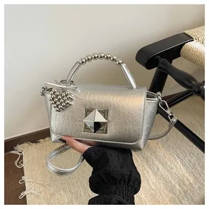 Detailed close-up view of silver metallic handbag featuring a beaded handle and heart charm