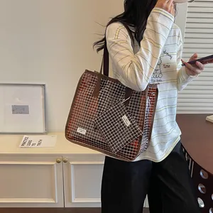 Model carrying a large brown grid tote bag with a small matching pouch in a minimal room