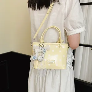 Pale yellow polka dot handbag with a musical note charm shown carried by a model