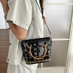 Close-up detail of black patent leather bucket bag with bamboo handles and sun embroidery
