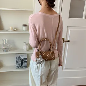 Brown polka dot cylindrical handbag styled as a crossbody bag on a model back view