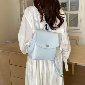 Rear view of a minimalist light blue leather backpack worn by a model in a white dress.