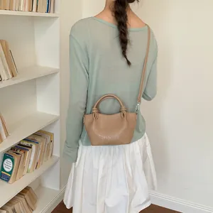 Back view of a woman wearing a tan bucket bag with knot details in a minimalist library setting.