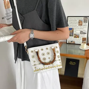 Detail of white quilted bucket bag with vintage bamboo handle and sun embroidery