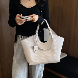 Detailed close-up of a beige woven tote bag being held by a model in a natural setting