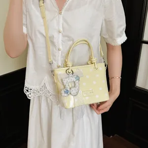 Detailed view of yellow polka dot handbag with decorative musical note pendant and lace.