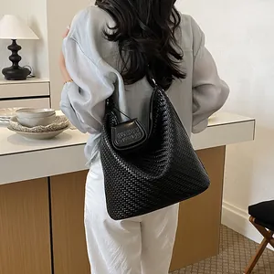 Woman wearing a black woven bucket bag in a minimalist interior setting.
