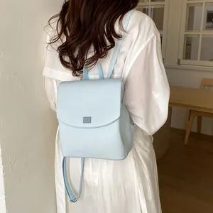 Back view of a stylish minimalist light blue leather backpack for women on a white dress