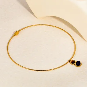 Close-up detail of a gold snake chain necklace with lapis lazuli and tiger eye pendants.