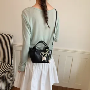 Back view of a minimalist black textured bucket bag with pearl bow charm on a model