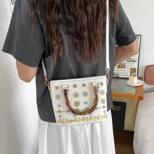 Stylish white bucket bag with bamboo handles and eye embroidery pattern shown on model