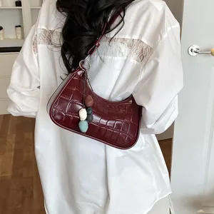Detail view of stylish burgundy crocodile texture dumpling shoulder bag on a model