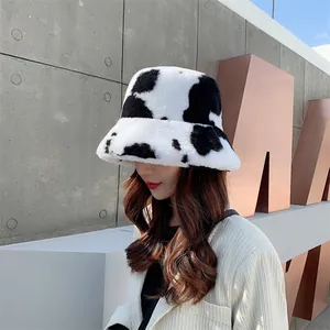 Cozy cow-print plush bucket hat worn by model against a stylish concrete background.