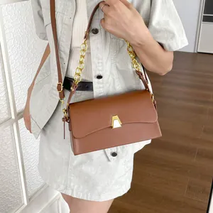Elegant brown rectangular crossbody bag with gold chain strap carried by a model