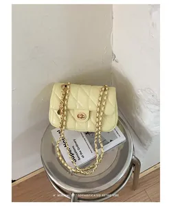 Detail van een gele doorgestikte tas met gouden ketting en sluiting op kruk.