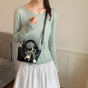 Detail of a black bucket bag featuring a pearl bow and tulip charm shown on a model