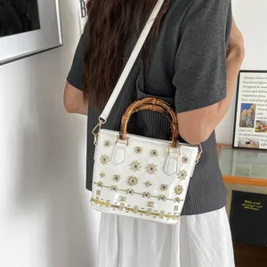 Elegant white bucket bag with bamboo handle and intricate floral patterns detail.