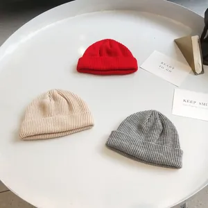 Detailed view of knitted beanies in red, beige, and grey colors on a clean white surface.