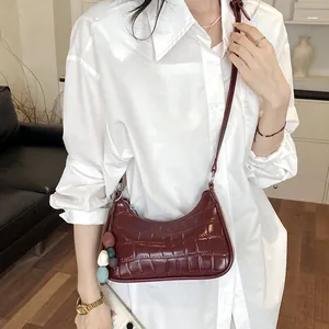 Detailed lifestyle view of a burgundy crocodile pattern dumpling bag with white shirt.