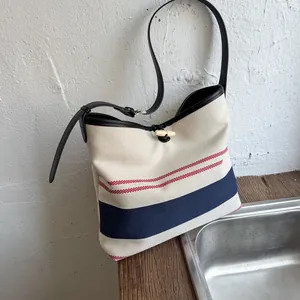 Detail view of striped canvas tote bag featuring a wooden toggle closure and leather strap.