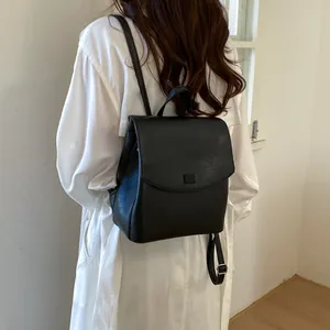 Rear view of a model wearing a minimalist black leather backpack with flap closure