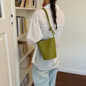 Detailansicht einer gewebten Eimertasche in Avocadogrün in gemütlicher Bibliothekskulisse.