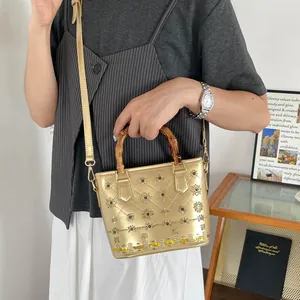 Chic gold metallic bucket bag featuring a natural bamboo handle and floral embroidery.